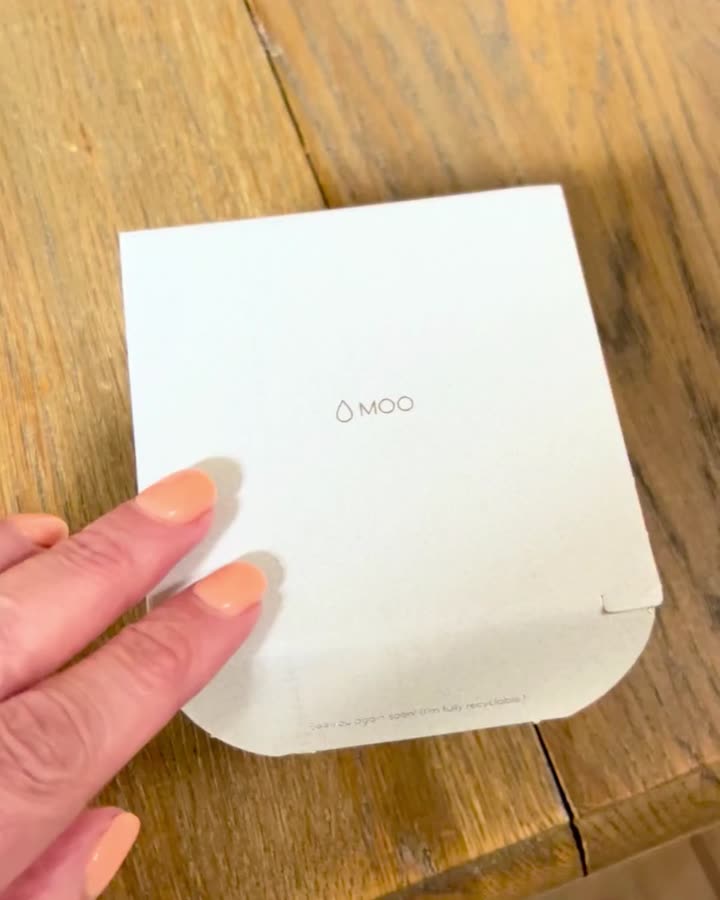 Hands opening a print box on a wooden table and lifting out the first Simple business cards — coral and navy, the goldfish-in-a-bowl mark on the back.